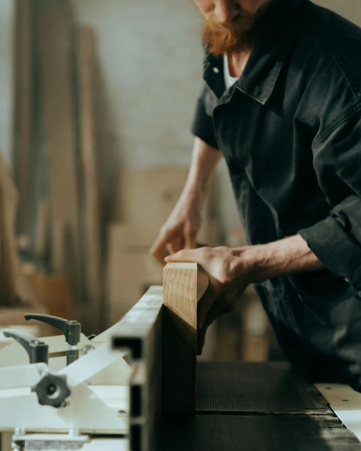 Mężczyzna pracuje nad drewnem w warsztacie stolarskim, używając narzędzi do obróbki drewna.